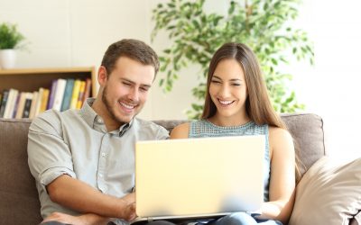 Front view portrait of a young happy couple using a laptop together sitting on a sofa in the living room at home